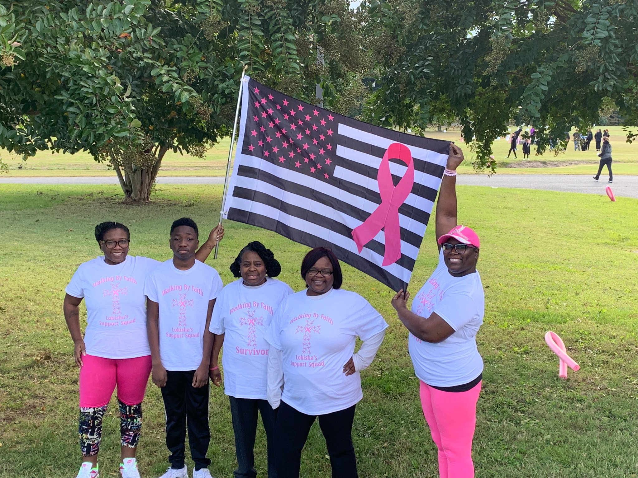 a group of people holding up a pink ribbon and an american flag