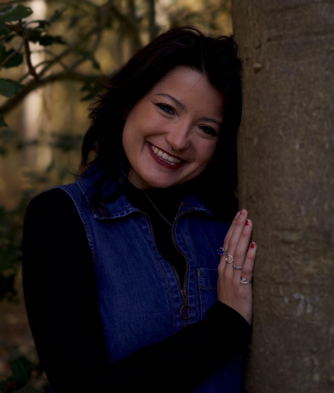 a woman leaning against a tree smiling for the camera